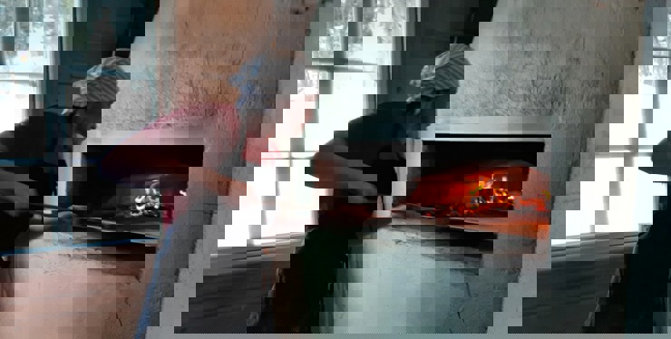 Bilden visar en person som skjutsar in ett tunnbröd i ugnen. Det syns hur det brinner i ugnen.